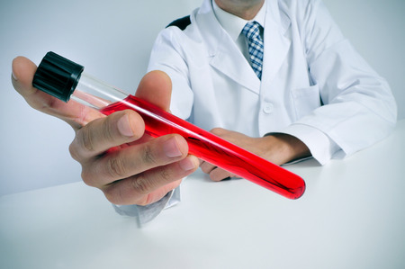 closeup of a young caucasian man wearing white coat sitting at his desk holds a blood sample in his handの写真素材