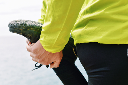 closeup of a young caucasian sportsman wearing sport clothes stretching his quadriceps before or after runningの写真素材
