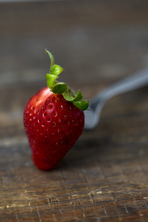 closeup of a ripe strawberry in a fork on a rustic wooden tableの写真素材