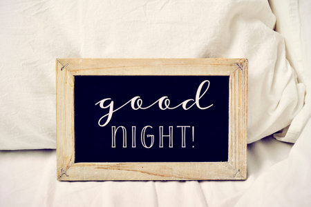 closeup of a wooden-framed chalkboard with the text good night written in it, placed on a comfortable bedの写真素材
