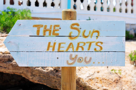 closeup of a white wooden signpost attached to a wooden pole with the text the sun hearts you...