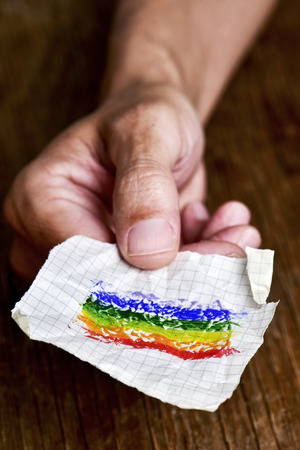 closeup of a young caucasian man with a piece of paper in his hand with a rainbow flag painted in itの写真素材