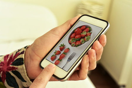 closeup of a young caucasian man with his smartphone ins his hands, with a picture of a bowl with strawberries, taken by myself, in its screenの写真素材