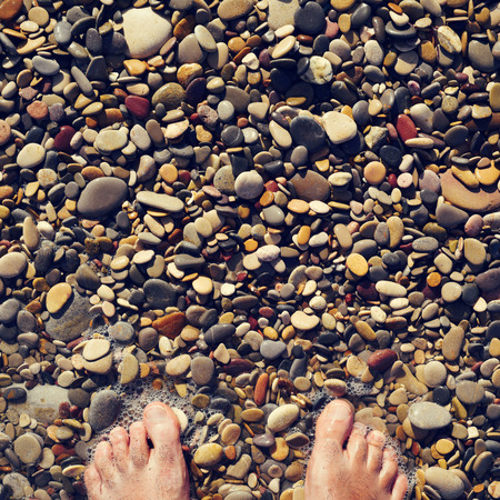 closeup of the feet of a young caucasian man in the seashore of a shingle beachの写真素材