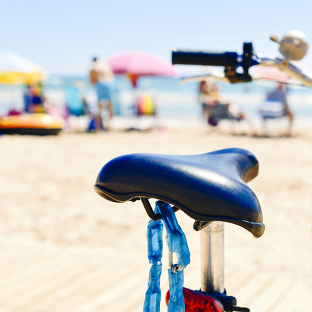 closeup of a bicycle parked a the seafront of a beach with unrecognizable people in the backgroundの写真素材