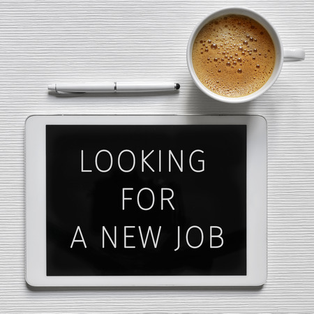 high-angle shot of a tablet computer with the text looking for a new job in its screen, a cup of coffee and a digital pen on a white surfaceの写真素材