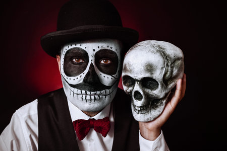 portrait of a young man with a mexican calaveras makeup, wearing bow tie and bowler hat, holding a...