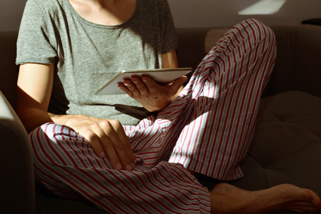 closeup of a young caucasian man in pajamas using a tablet computer seating in a couchの写真素材