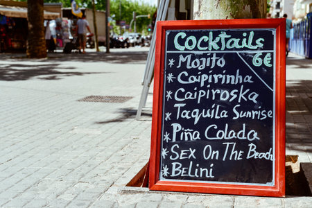 a menu chalkboard with a list of cocktails in front of a restaurant in a pedestrian street in Barcelona, Spain, with drinks like mojito caipirinha, caipiroska, pina colada or sex on the beachのeditorial素材
