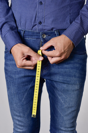 closeup of a young man holding a long piece of measuring tape that is popping up from the fly of his jeansの写真素材