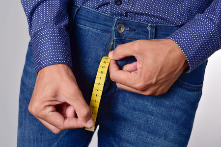 closeup of a young man holding a piece of measuring tape that is popping up from the fly of his...