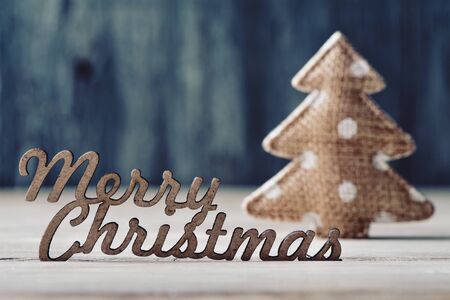 the text merry christmas made in wooden and a cozy ornament in the shape of a christmas tree on a rustic wooden surfaceの写真素材