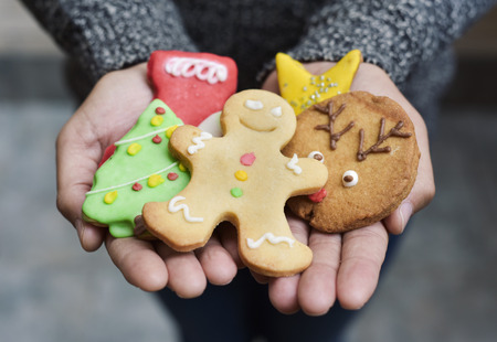 closeup of a young caucasian man with a pile of christmas cookies with different shapes and colors in his handsの写真素材