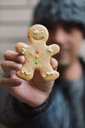 closeup of a young caucasian man wearing a knitted cap holding a gingerbread man in his hand in...