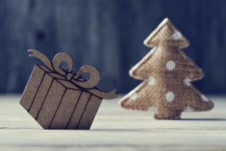 a wooden ornament in the shape of a gift and a jute fabric christmas tree on a rustic wooden surfaceの写真素材