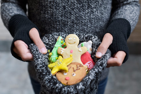 closeup of a young caucasian man wearing mittens holding in his hands a knitted stocking full of christmas cookies with different shapes and colorsの写真素材