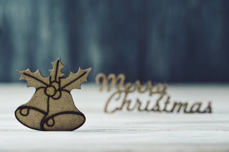 the text merry christmas made in wooden and a wooden ornament in the shape of a pair of bells and a twig of christmas holly, on a rustic wooden surfaceの写真素材