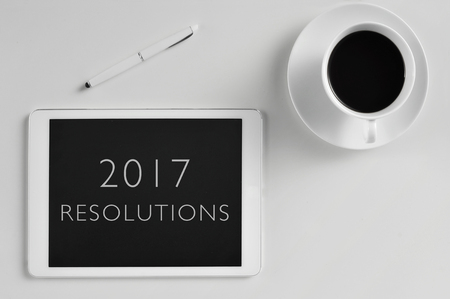 high-angle shot of a tablet with the text 2017 resolutions in its screen, a pen and a cup of coffee, on an off-white surfaceの写真素材