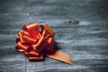 an orange satin gift ribbon bow on a rustic wooden surface, with a negative spaceの写真素材