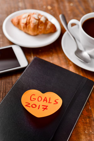 an orange heart-shaped sticky note with the text goals 2017 written in it attached to a black...