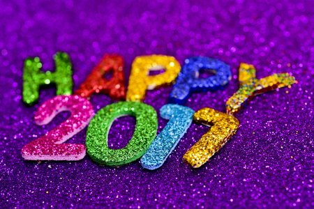closeup of some glittering letters of different colors forming the text happy 2017, on a violet glittering backgroundの写真素材