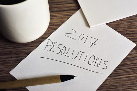 a pen and a piece of paper with the text 2017 resolutions handwritten in it on a rustic wooden table next to a cup of coffee の写真素材