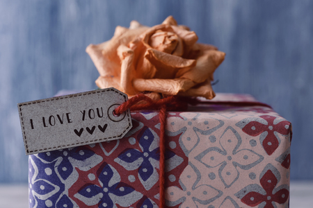 closeup of a gift topped with an artificial flower and with a paper label with the text I love you tied to it with a red stringの写真素材