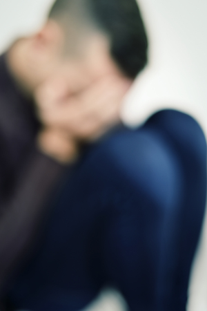 closeup of a blurred young caucasian man curled up with his hands in his faceの写真素材