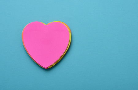a stack of heart-shaped sticky notes of different colors topped by a pink one with a blank space in it on a blue background with a blank space at the rightの写真素材