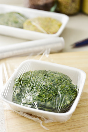 closeup of some different raw veggie burgers in plastic trays covered with plastic wrap ready to be introduced in the fridge or in the freezerの写真素材