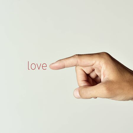 closeup of the forefinger of a young caucasian man pointing the word love, against an off-white backgroundの写真素材