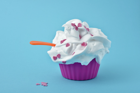 closeup of a pink plastic cup full of a white ice cream topped with pink heart-shaped confetti sprinkles on a blue backgroundの写真素材