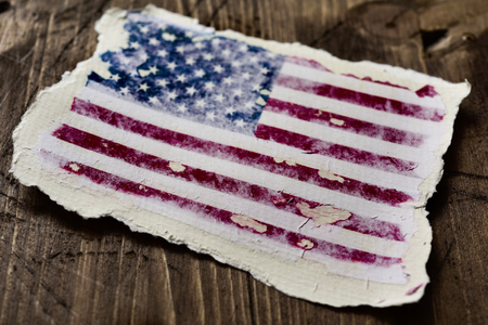 the flag of the United States in an aged piece of paper on a rustic wooden backgroundの写真素材