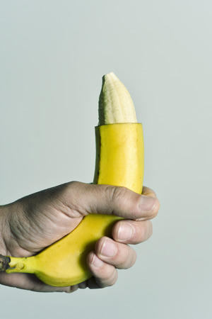 closeup of the hand of a young man with a banana with the tip of its skin removed, depicting a circumcised male memberの写真素材