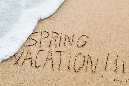 closeup of the text spring vacation written in the sand of a beach