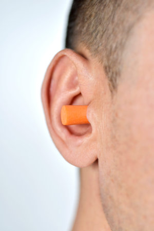 closeup of a young caucasian man with an orange earplug inserted in his ear