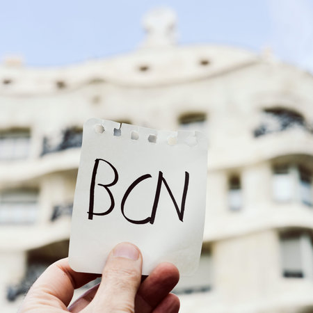 closeup of the hand of a young caucasian man holding a note with the word BCN, for Barcelona, written in it, in front of La Pedrera, in Barcelona, Spainの写真素材