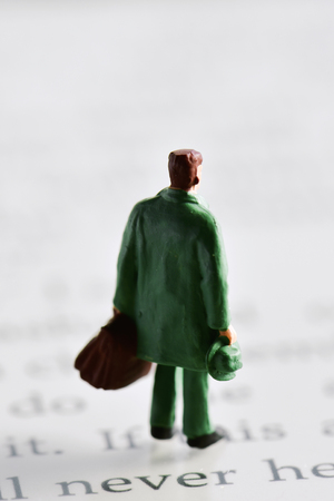 miniature traveler man seen from behind carrying a suitcase and a hat placed on an e-book readerの写真素材