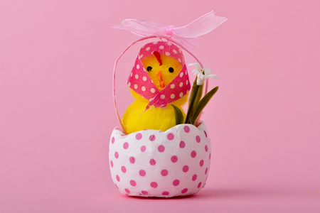 a funny lady teddy chick wearing a pink headscarf patterned with white dots emerging from a cracked white eggshell patterned with pink dots, against a pink background with a blank space around itの写真素材