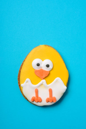 closeup of a cookie decorated as a yellow chick emerging from a cracked egg against a blue...