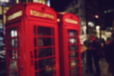 a defocused blur background of people walking in a street at night in London, United Kingdom, with two typical red telephone booths in the foregroundの写真素材