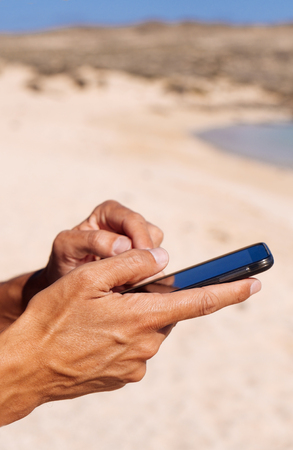 closeup of a young caucasian man using a smartphone on a white sand beach next to the seaの写真素材
