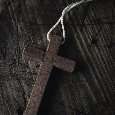 closeup of a small wooden cross with a cord tied to it, on a rustic wooden surfaceの写真素材