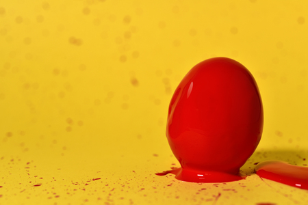 an egg covered by red paint placed on a yellow background splashed by the same paintの写真素材
