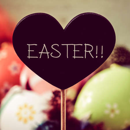 closeup of a heart-shaped black chalkboard with the text easter written in it and pile of different decorated easter eggs and feathers of different colors in the backgroundの写真素材