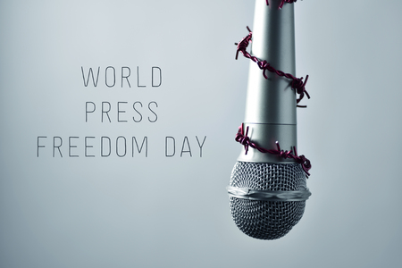 closeup of a microphone encircled by a red barbed wire and the text world press freedom day on a gradient gray backgroundの写真素材