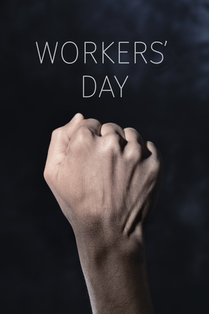 closeup of the raised fist of a young man against a gradient dark gray background and the text workers dayの写真素材