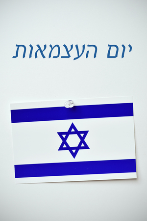 the text day of israel written in hebrew and an israeli flag pinned with a push-pin to an off-white backgroundの写真素材