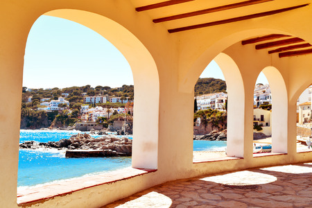 a view of the the Barques Beach and the coast of Calella de Palafrugell, in the Costa Brava, Catalonia, Spain, seen through the arches of the characteristics porticos of its white housesの写真素材