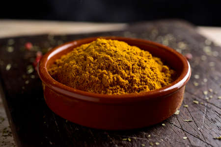 closeup of an earthenware bowl full of curry powder, on a rustic wooden chopping board, on a tableの写真素材